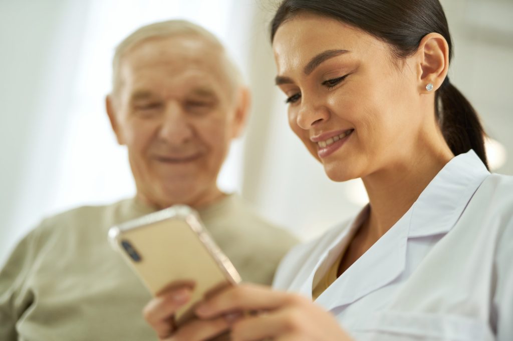 Smiling nurse and senior citizen looking at smartphone screen